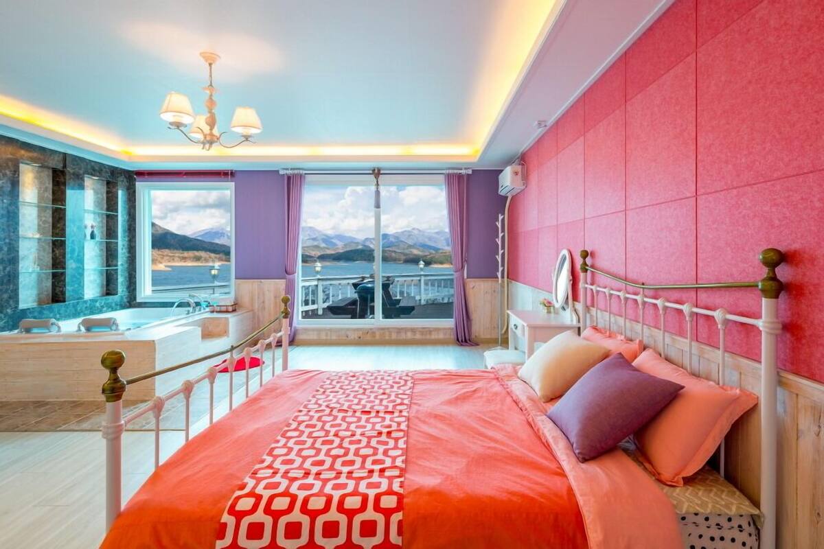 A bedroom with a large bed, a view of mountains and a lake, a bathroom with a bathtub, and a chandelier.
