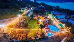 A well-lit outdoor area with a swimming pool, a stone pathway, and a house with a visible deck and outdoor seating area. - Hosu Ilchul Pension (Jecheon)