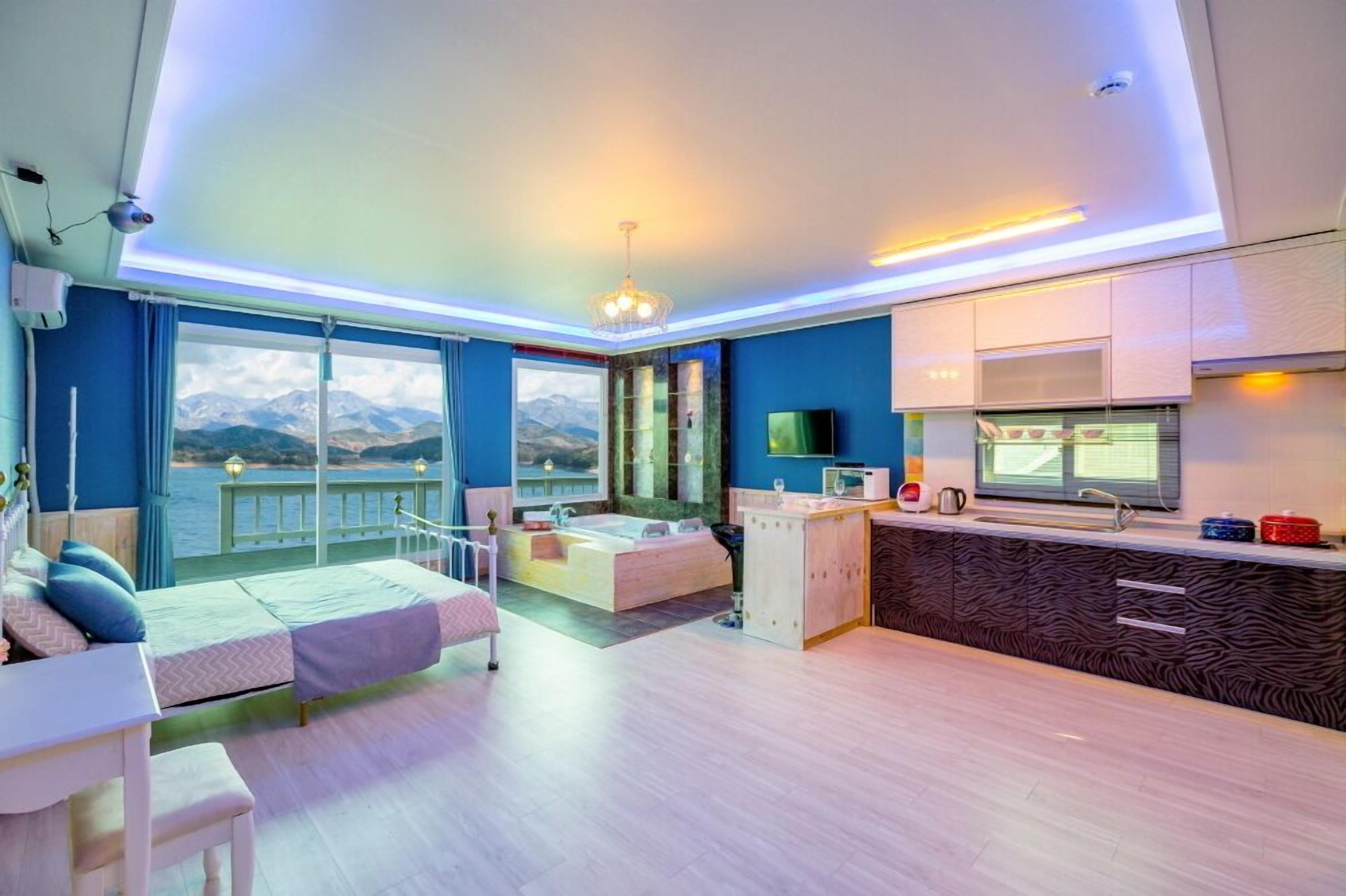 Una habitació moderna amb una finestra gran, un balcó, un llit, un rentaplat i una zona de cuina.