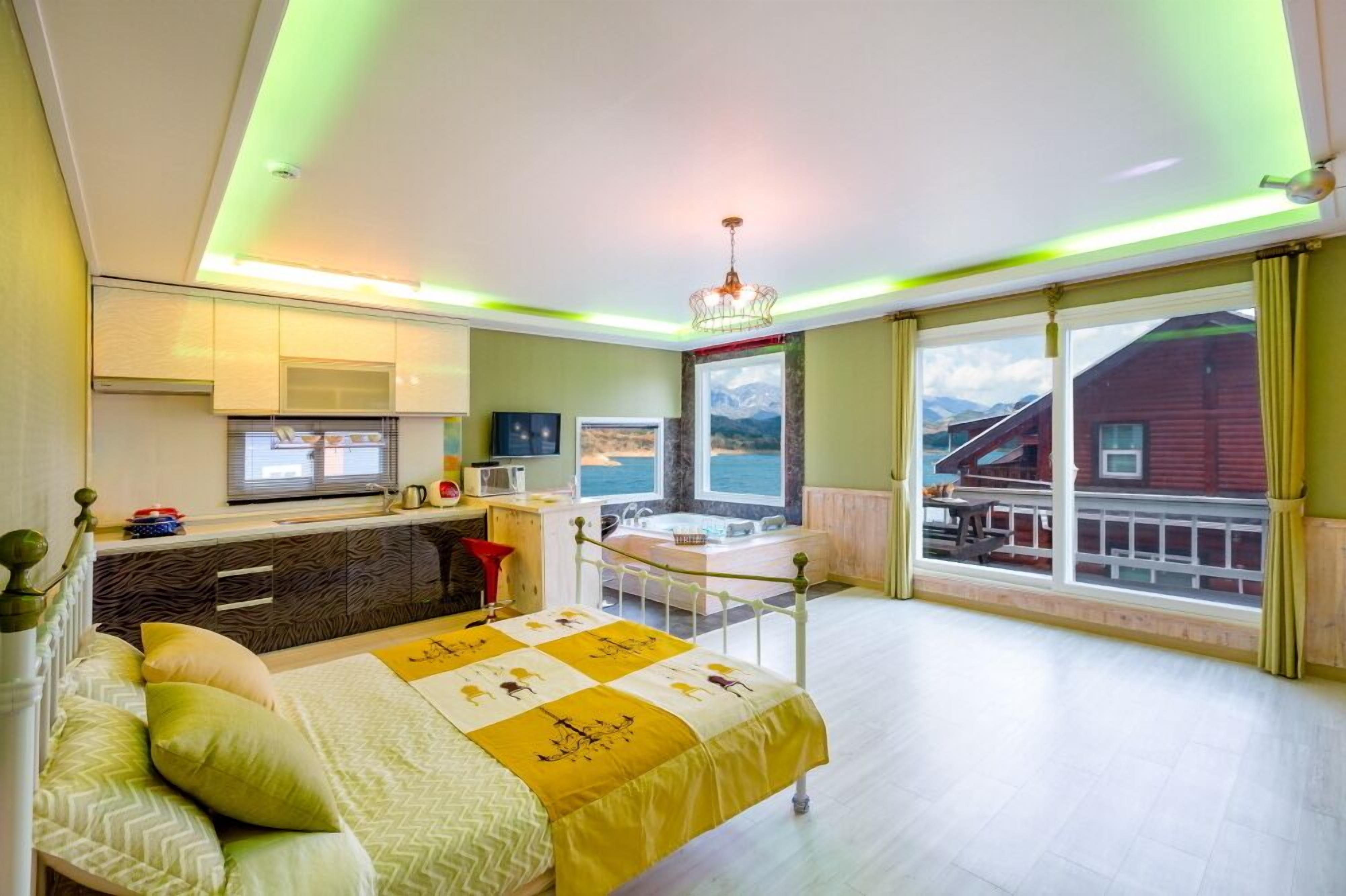 A bedroom with a bed, a desk, a window with a view of mountains, and a balcony.