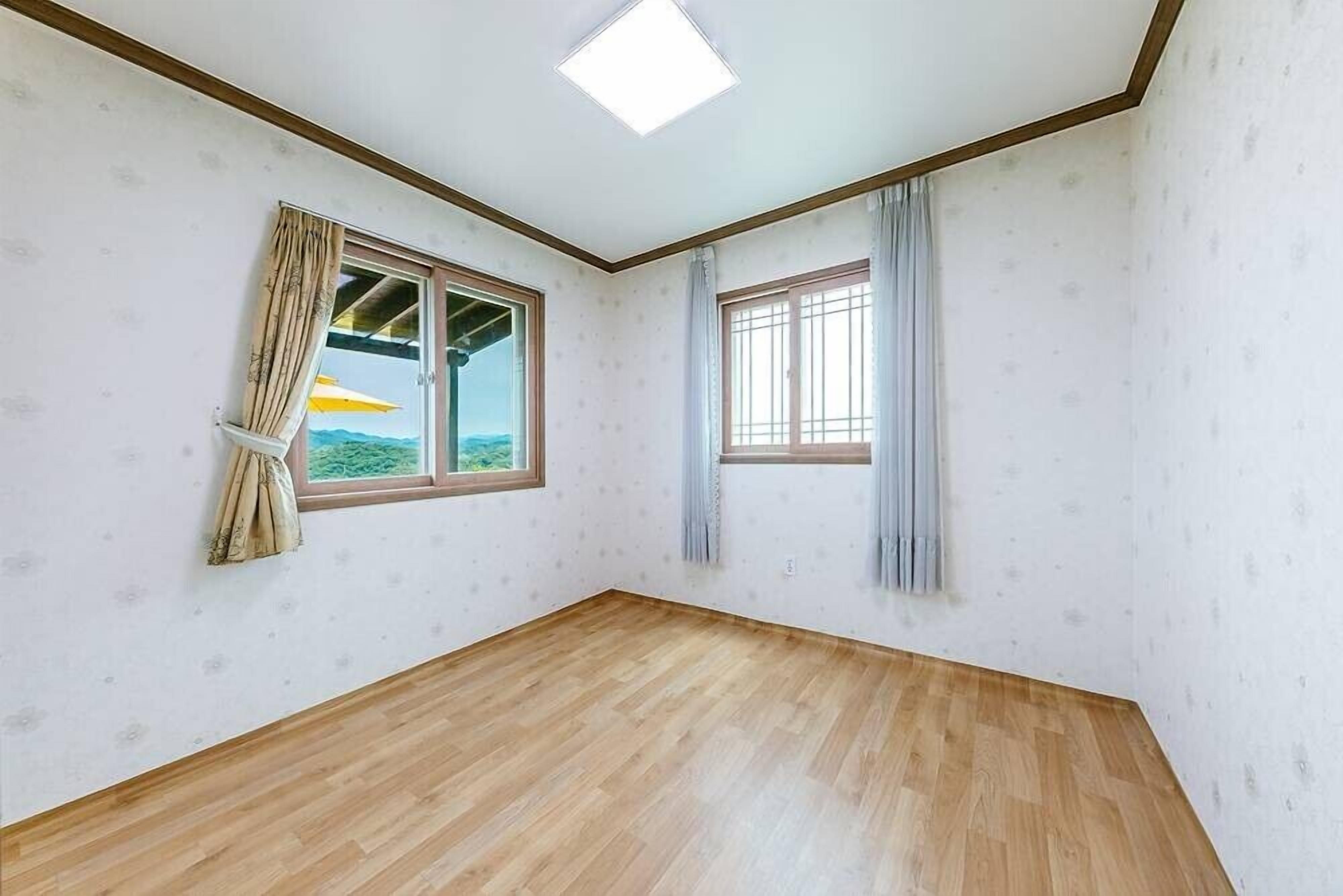 A room with two windows, wooden flooring, and a ceiling light.