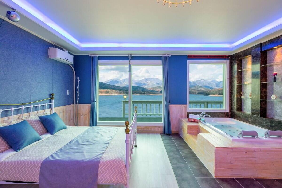 A bedroom with a bed, a window with a view of the sea, and a bathroom with a bathtub.