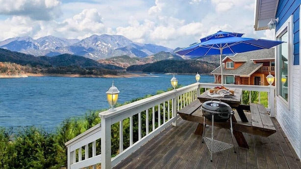 A deck with a grill, a table, and a blue umbrella overlooking a lake with mountains in the background. - Hosu Ilchul Pension (Jecheon)