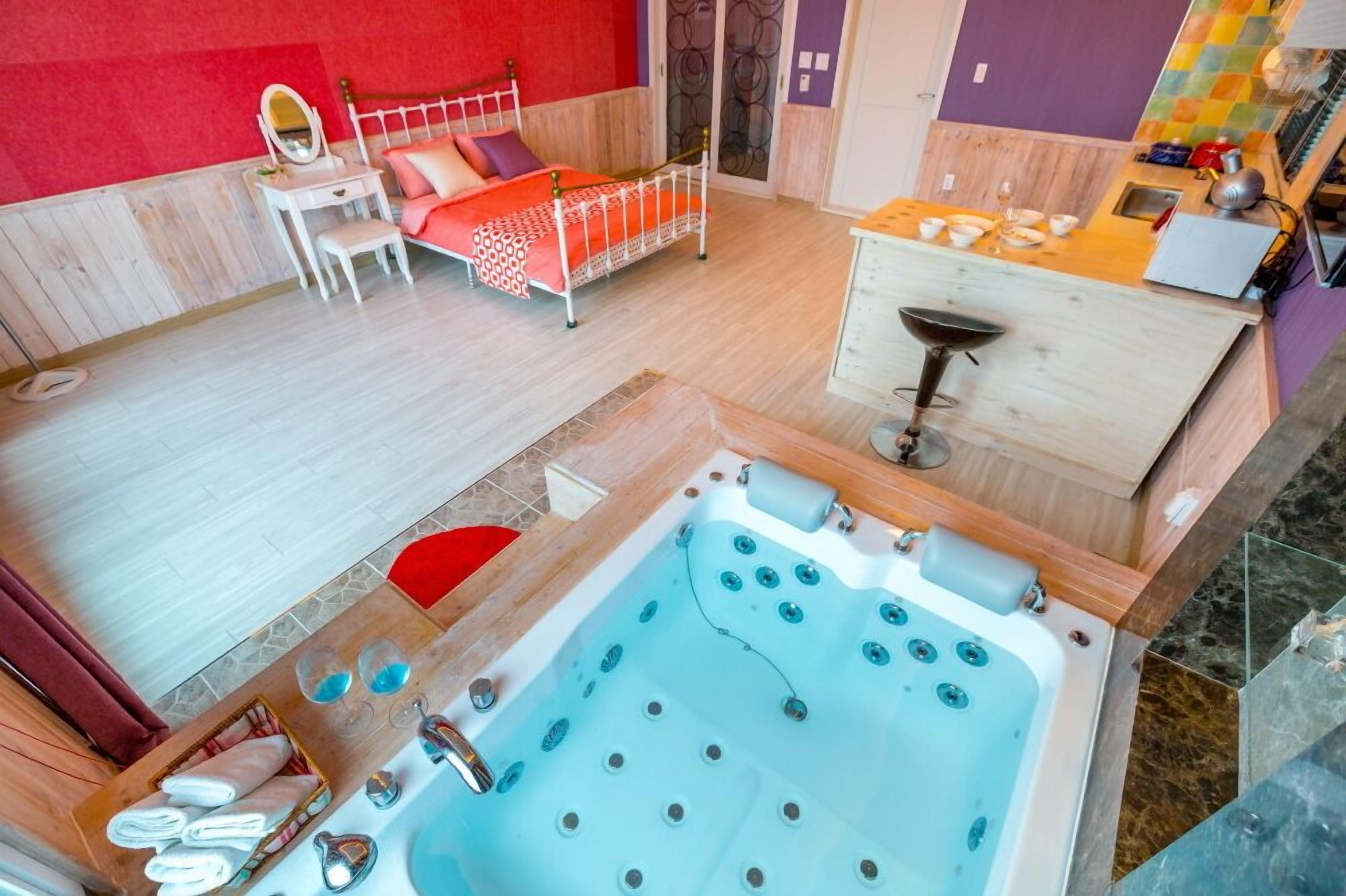 Una habitación con cama, escritorio, tocador, una pequeña mesa con vasos y una bañera.