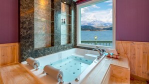 A large bathtub with a view of a lake and mountains, wooden paneling, and glass shelves. - Hosu Ilchul Pension (Jecheon)