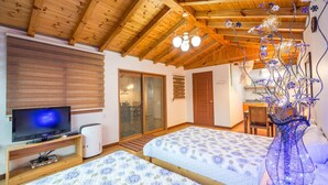 A cozy room with wooden beams, two beds with floral bedding, a TV, and a decorative vase.