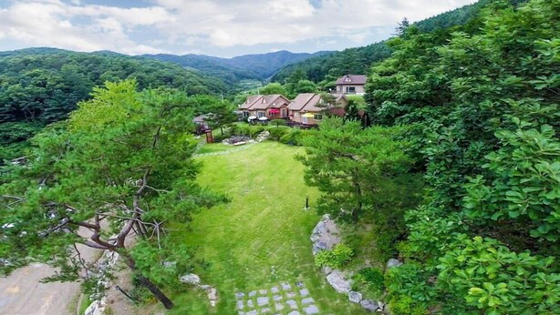 A residential area with houses surrounded by lush greenery and mountains in the background.