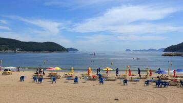 A beach with rows of blue chairs and umbrellas, a sandy shore, and calm water with boats.
