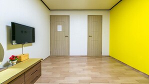 Una habitación con una televisión sobre un mueble bajo, un aparador de madera y dos puertas.