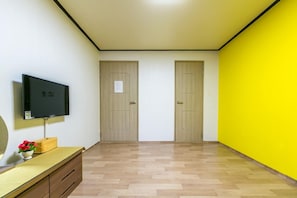 Una habitación con una televisión sobre un mueble bajo, un aparador de madera y dos puertas.