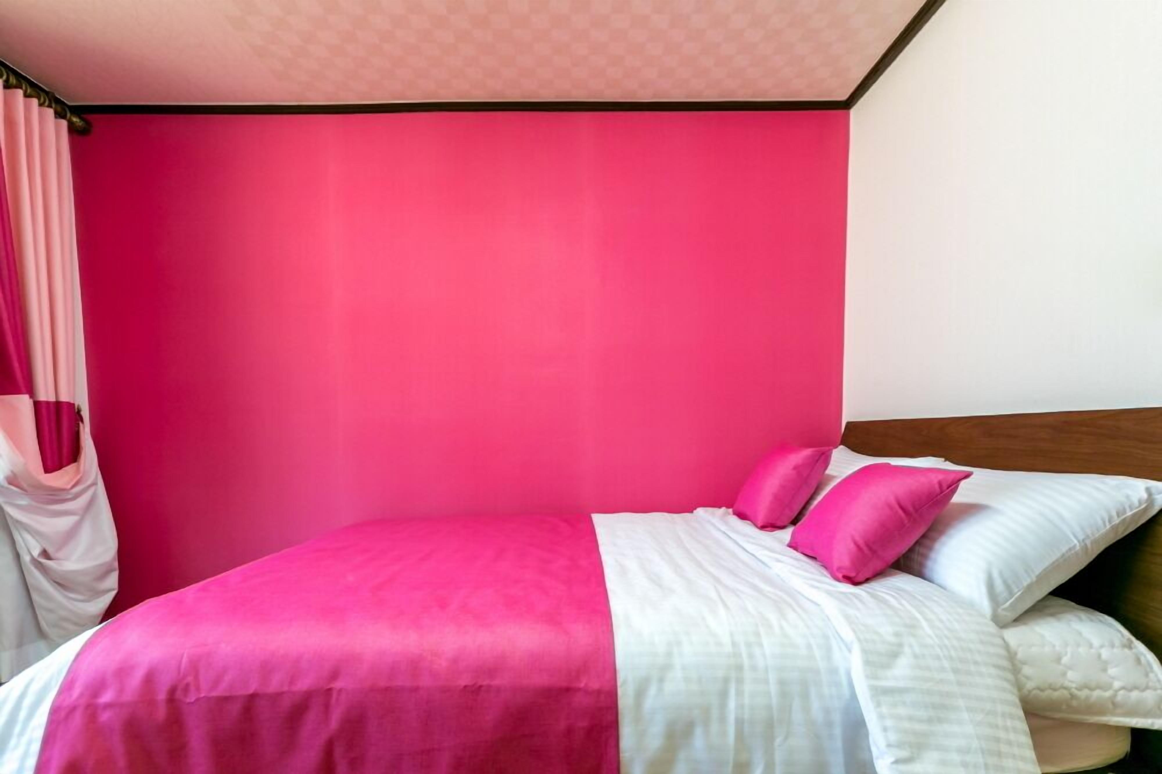 Una cama con ropa de cama rosa y blanca, un cabecero de madera y una cortina rosa.