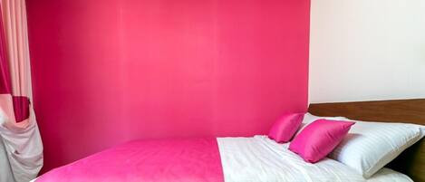 Una cama con ropa de cama rosa y blanca, un cabecero de madera y una cortina rosa.
