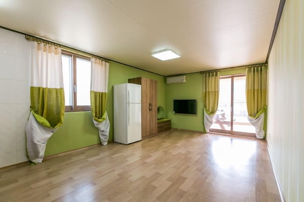 A room with a wooden floor, a white refrigerator, a wooden cabinet, a flat-screen TV, and a sliding glass door leading to a balcony. - Gatnaeum Pension (Geoje)