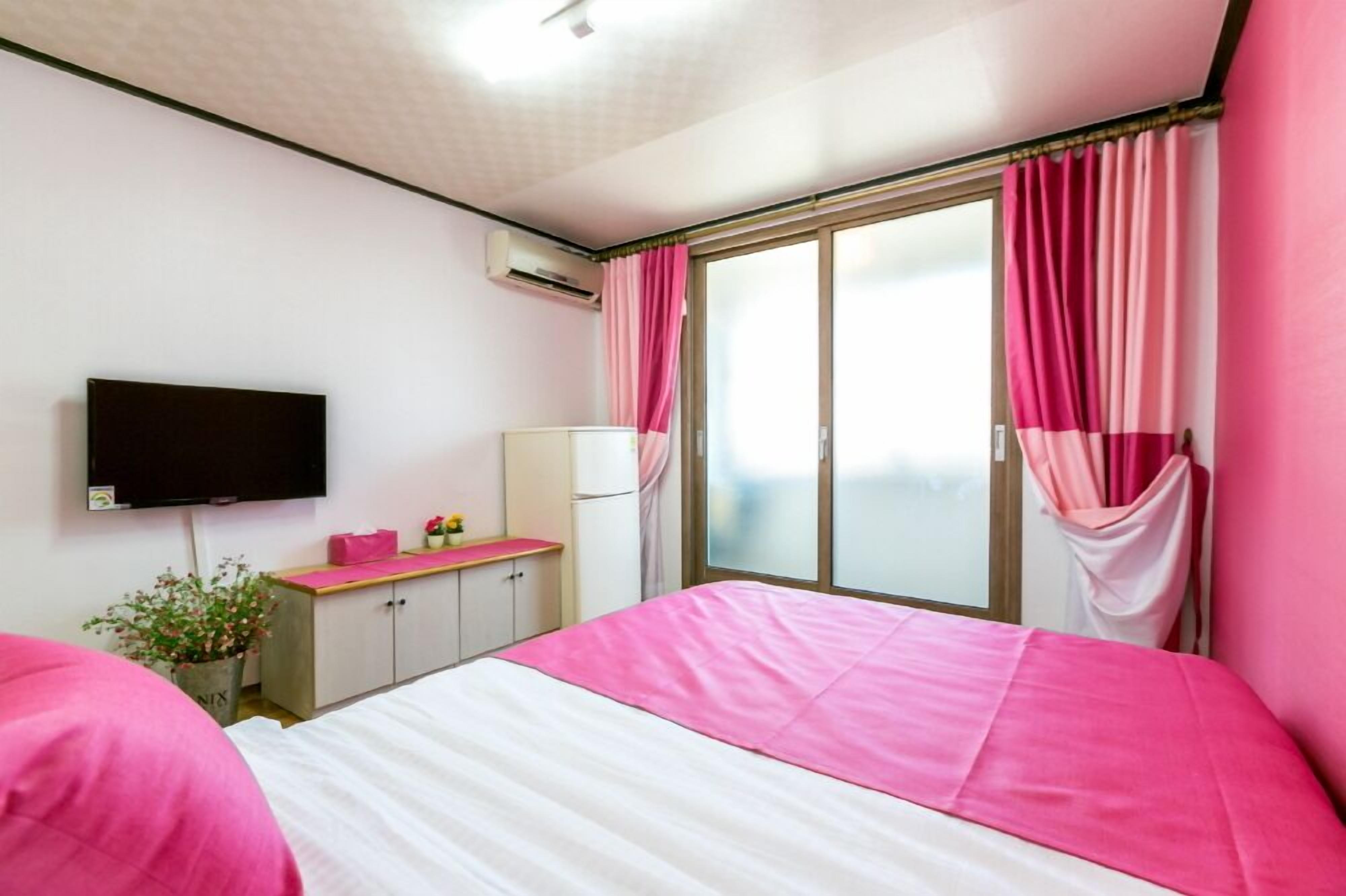 Quarto com cama, TV, escrivaninha e janela com cortinas.