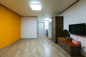 A hallway with a wooden floor, a white door at the end, a wooden cabinet with a TV on the wall, and a bright ceiling light. - Gatnaeum Pension (Geoje)