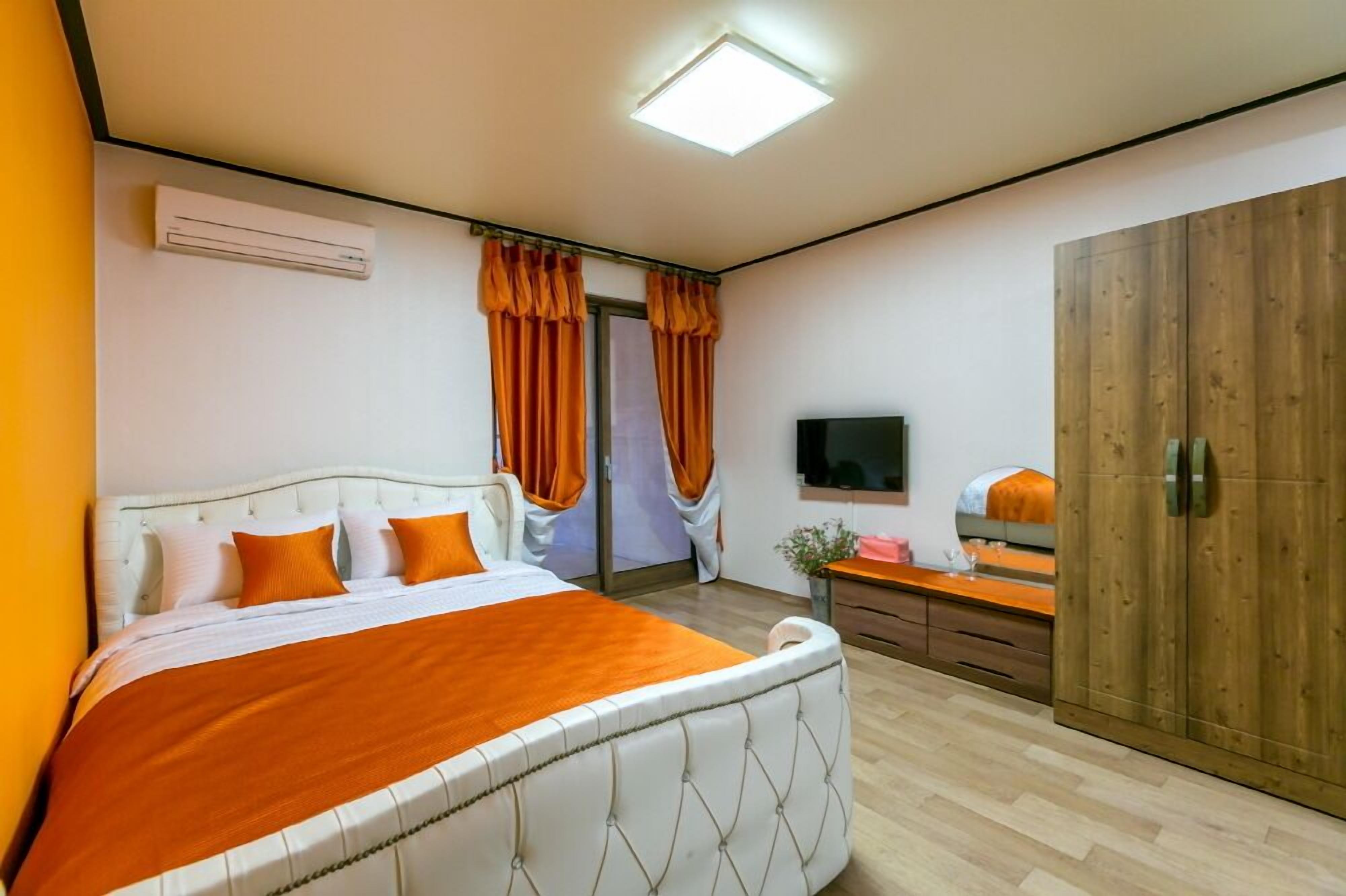 A bedroom with a bed, curtains, a TV, a wardrobe, and a bedside table.