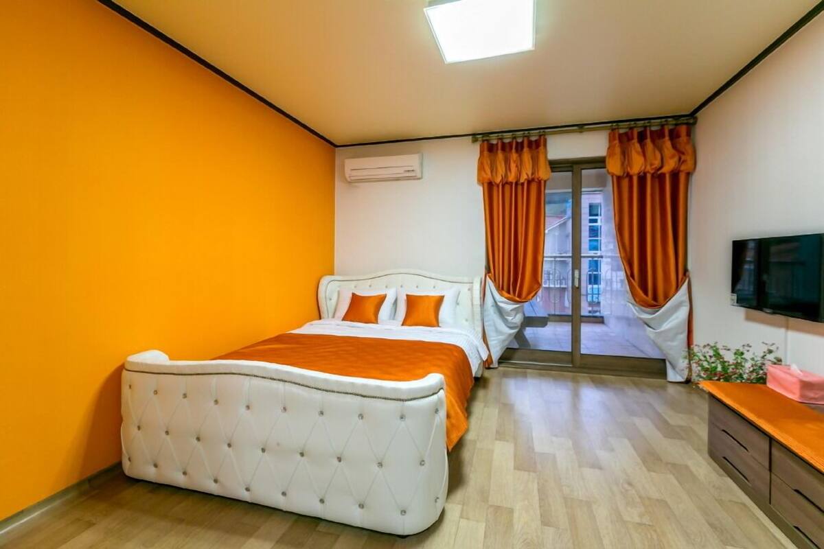 A bedroom with a bed, a TV, and a window with curtains.
