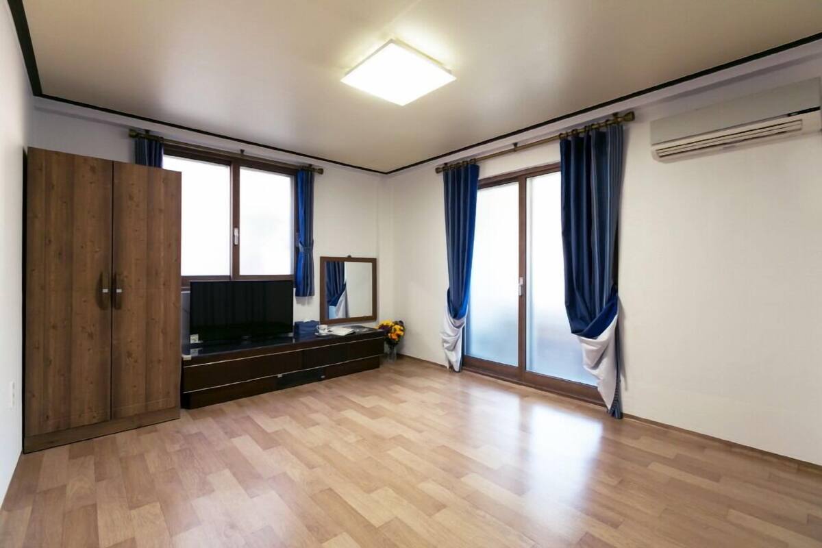 A room with a wooden floor, a TV, a mirror, and a wardrobe.