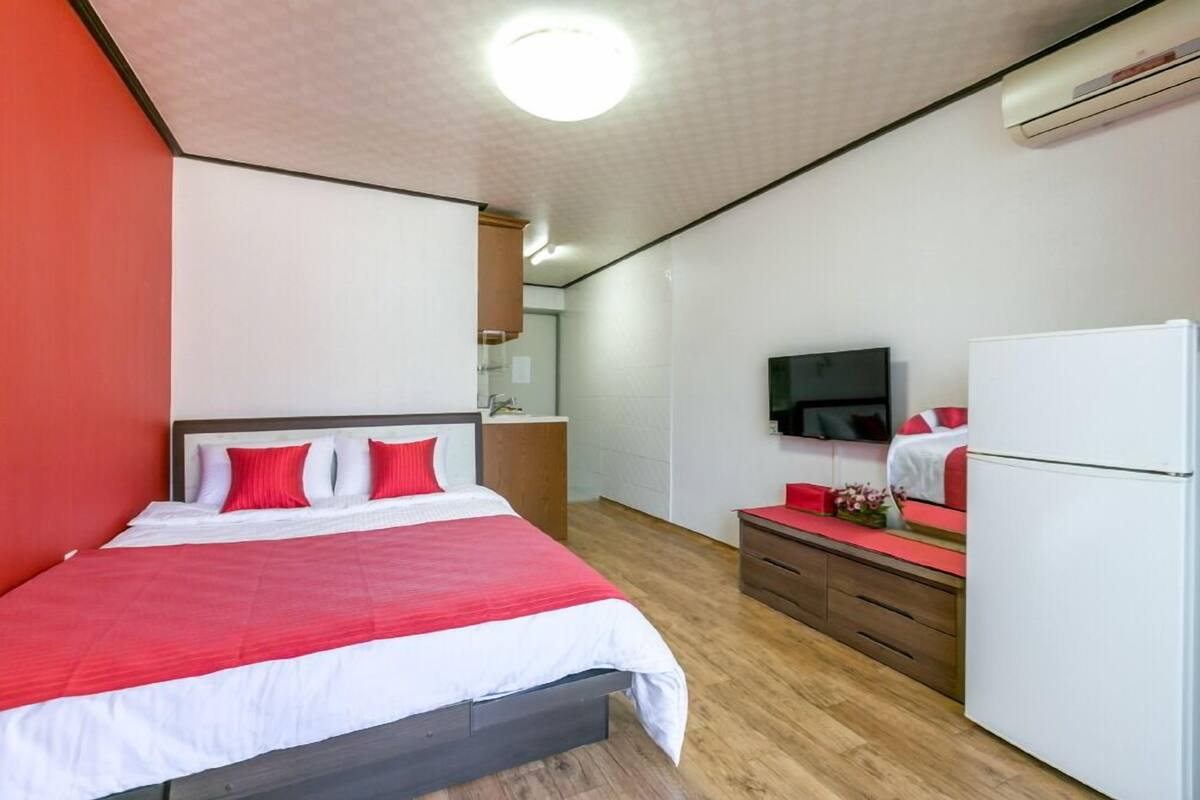 A hotel room with a bed, a dresser, a television, and an air conditioning unit.