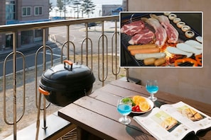 A balcony with a grill, a barbecue, and a table with a magazine, fruit, and a cocktail. - Gatnaeum Pension (Geoje)