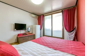 Un dormitorio con cama, cómoda, televisor y ventana con cortinas.