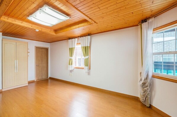 A spacious room with wooden flooring, a skylight, a wardrobe, and a window with curtains. - Gaejul Trip Pension (Geoje)