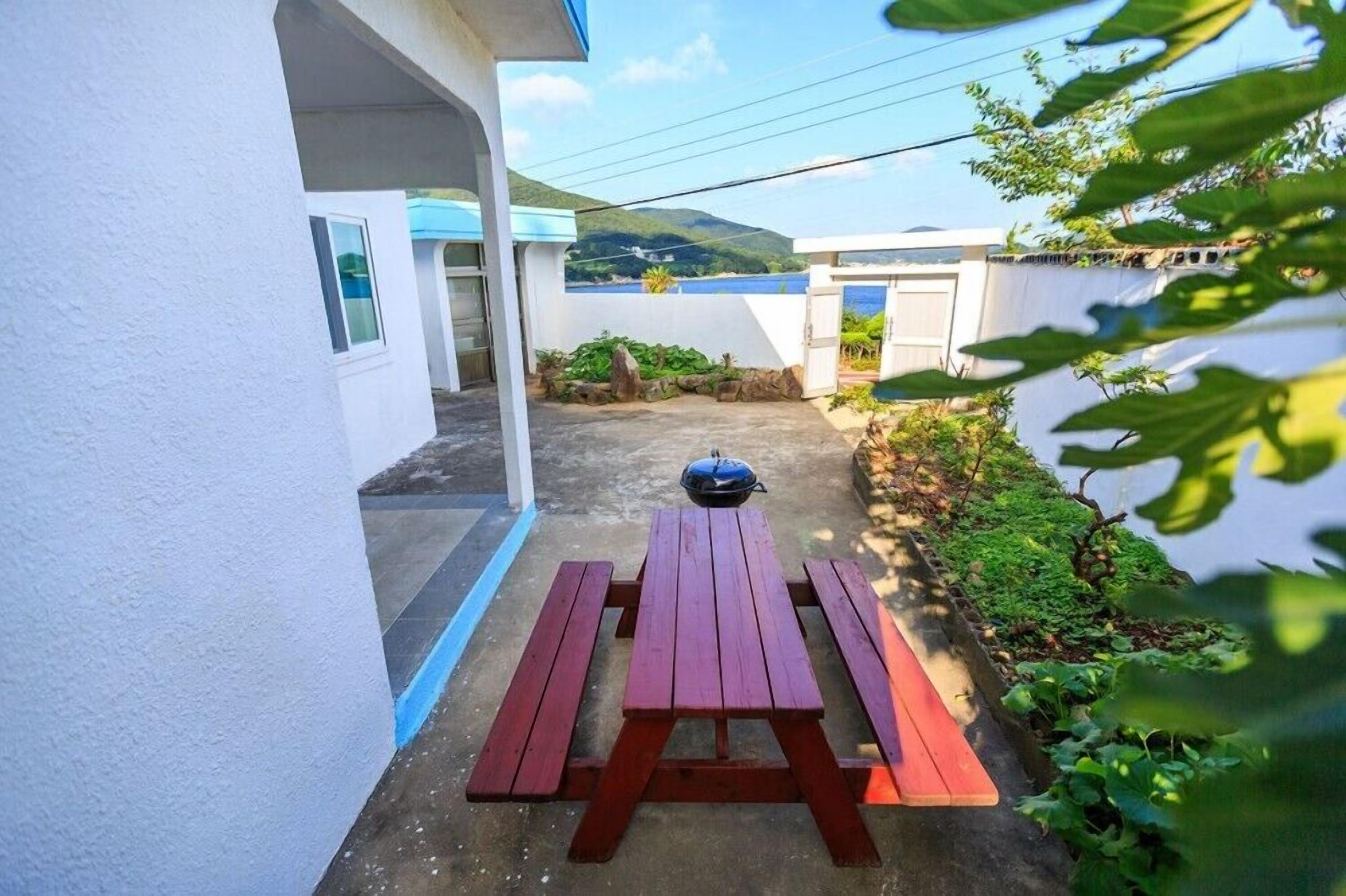 A patio area with a picnic table and a barbecue grill, surrounded by greenery and a view of a body of water and hills.