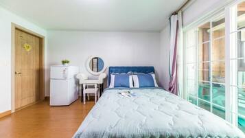 A bedroom with a bed, a desk, a chair, a small refrigerator, and a window with curtains.