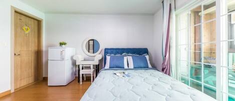 Een slaapkamer met een bed, een bureau, een stoel, een kleine koelkast en een raam met gordijnen.