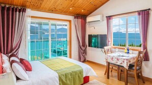 A bedroom with a bed, a dining table with chairs, a TV, and a balcony with a view. - Gaejul Trip Pension (Geoje)