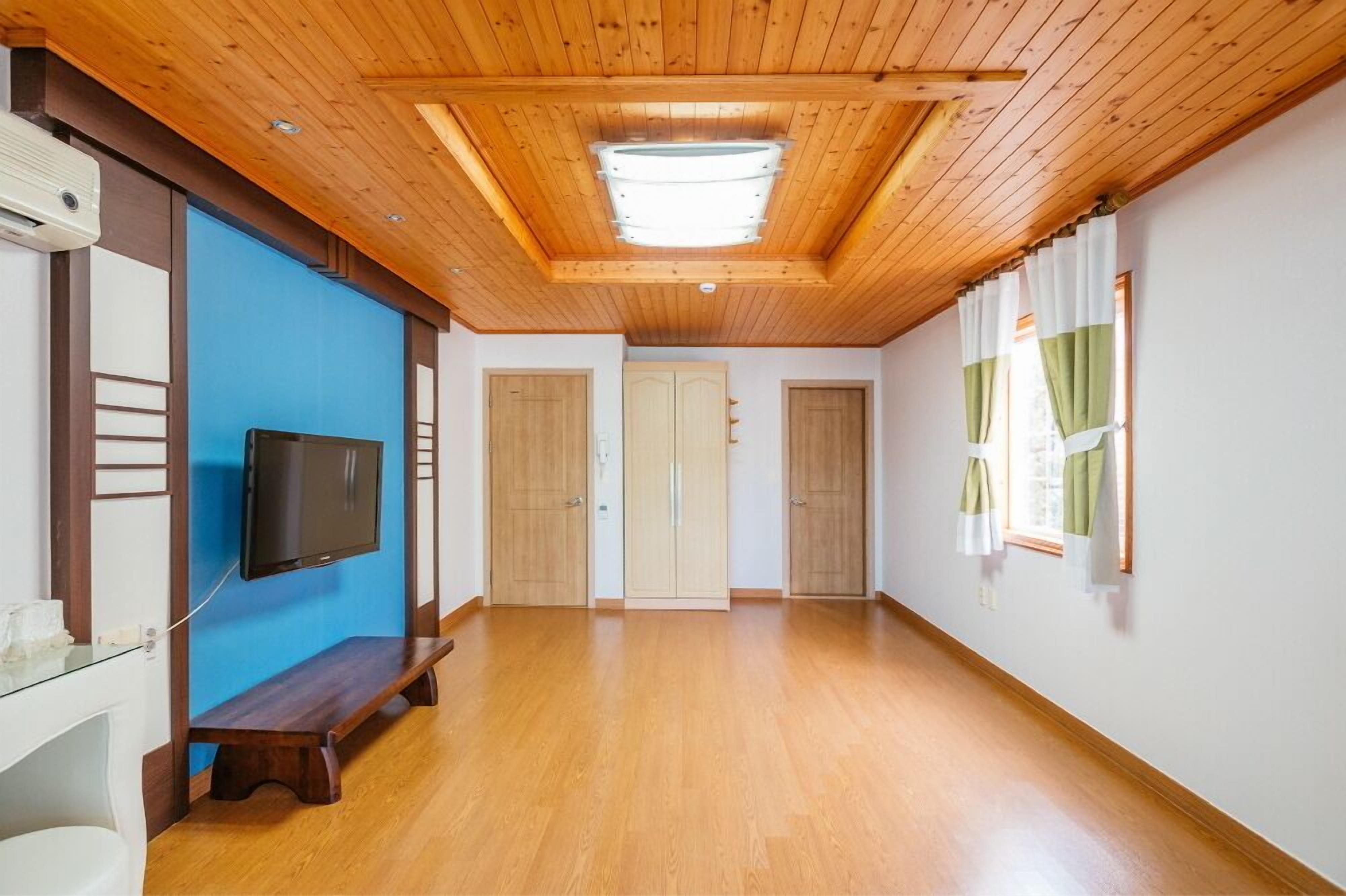 A spacious room with wooden flooring, a ceiling fan, a mounted TV, and a bench.