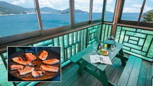 A balcony with a table set for two, overlooking a scenic ocean view. - Gaejul Trip Pension (Geoje)