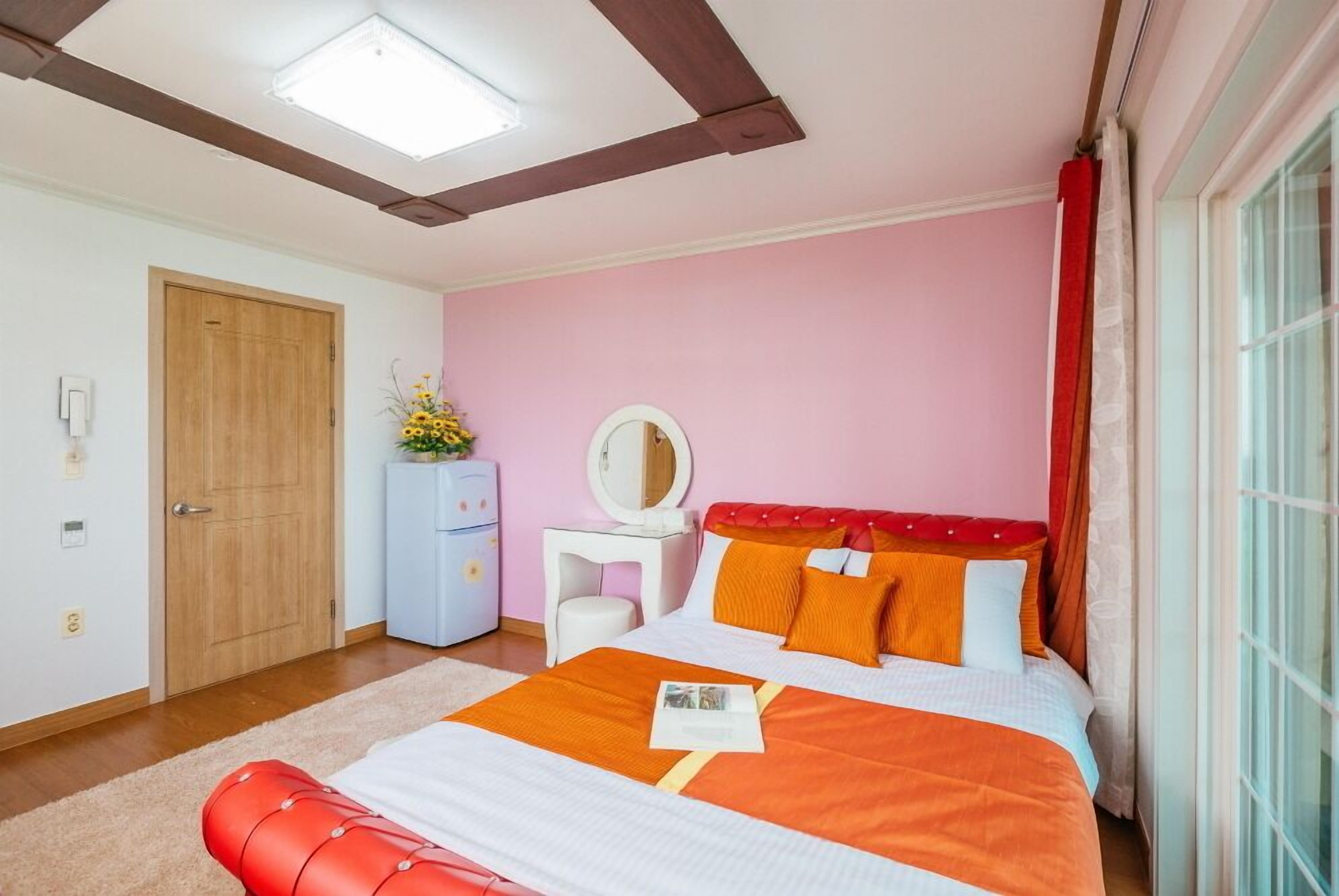 A bedroom with a bed, a dresser, a mirror, and a window with curtains.