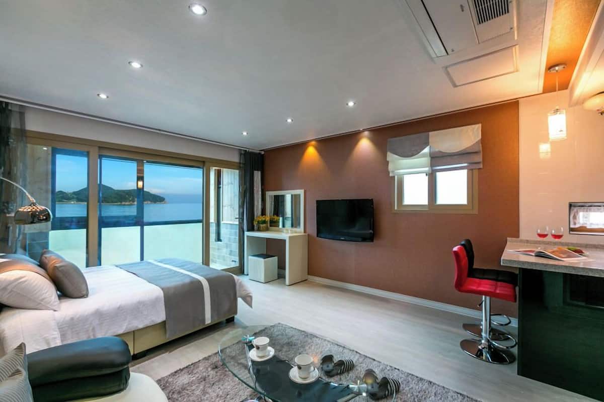 Una habitación de hotel moderna con una cama, un escritorio, un televisor y vistas al mar.