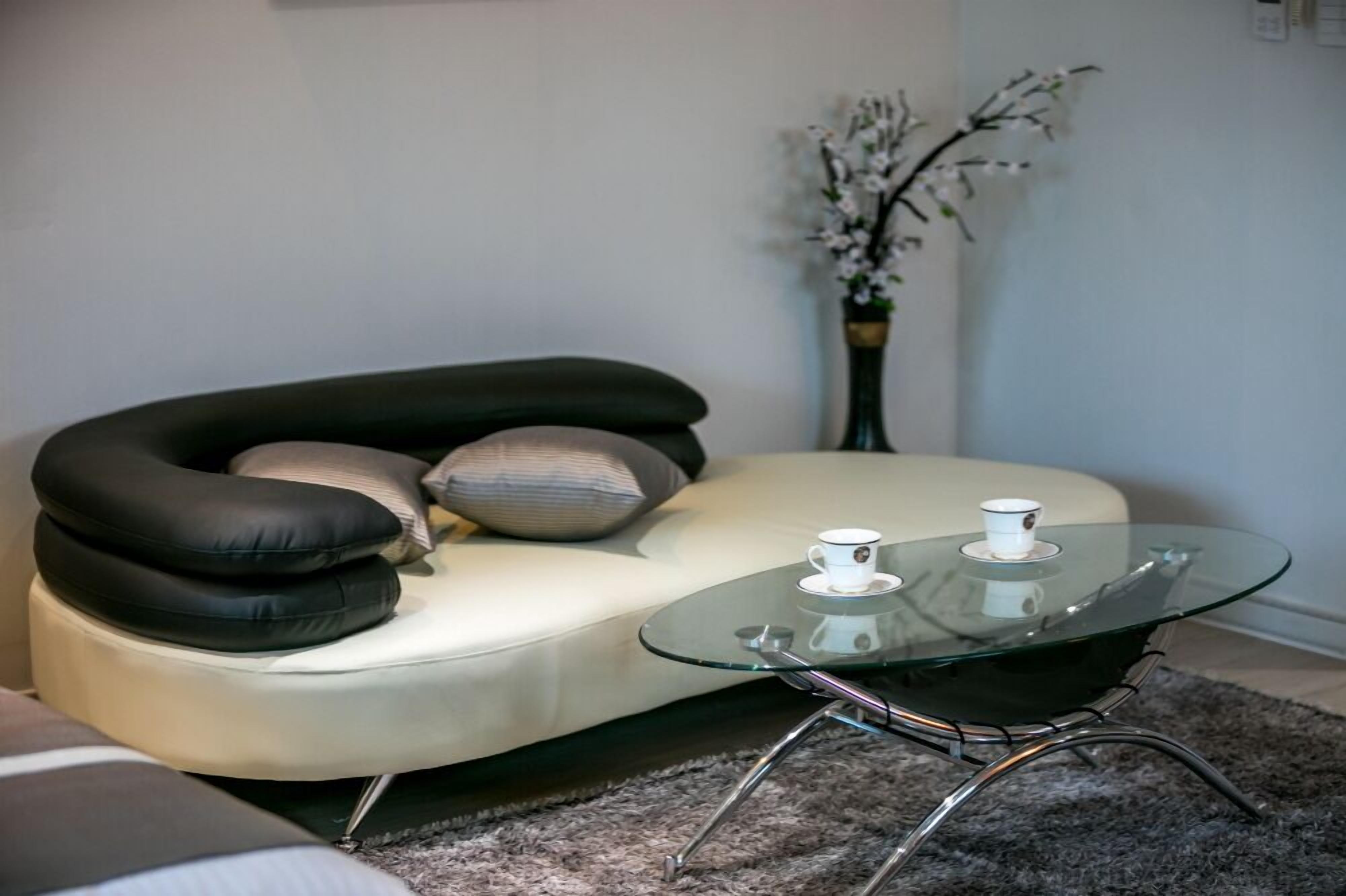 A modern living room with a curved sofa, a glass coffee table, and a vase with flowers.