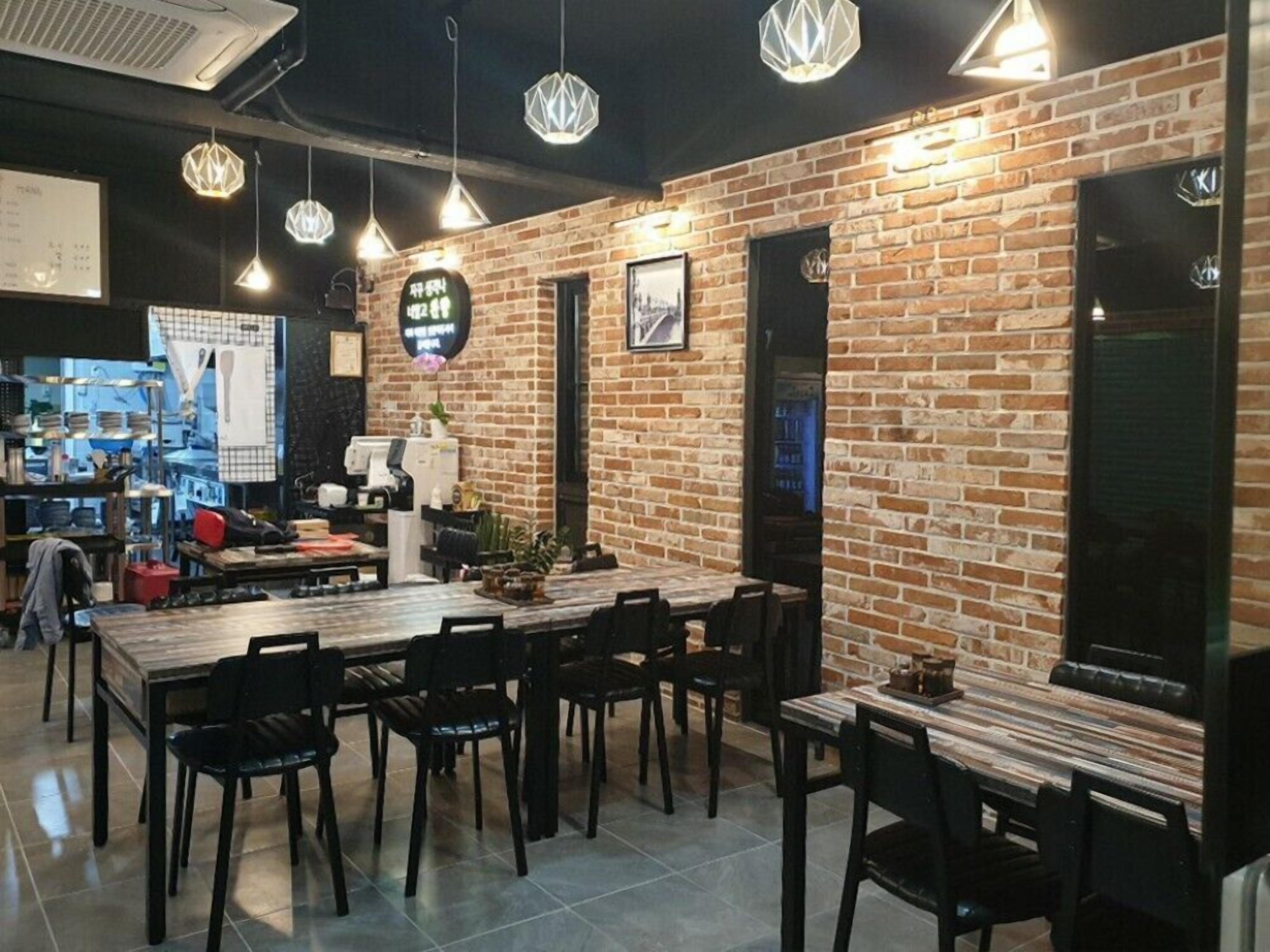 Un restaurante con paredes de ladrillo, lámparas colgantes y una zona de cocina a la vista.