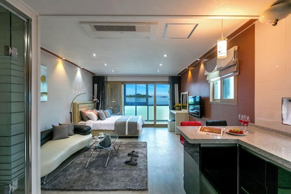 A modern hotel room with a bed, sofa, dining area, and large windows. - Goun Pension (Geoje)