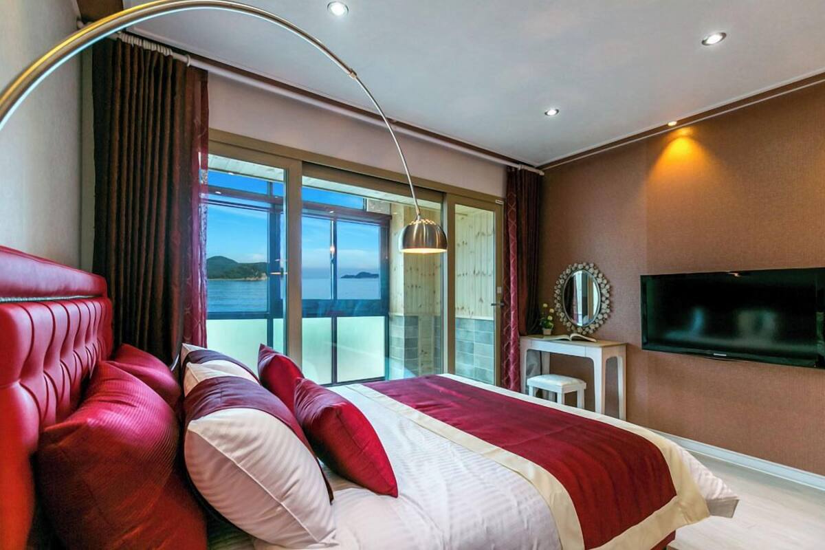 Habitación de hotel con una cama grande, un sofá rojo, un televisor y un balcón con vistas.