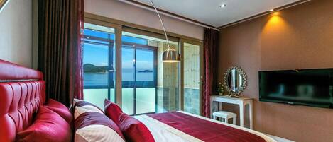 Een hotelkamer met een groot bed, een rode bank, een televisie en een balkon met uitzicht.
