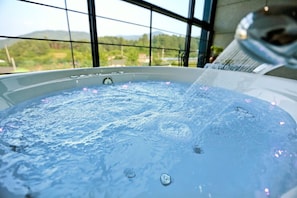 Un jacuzzi con vistas a un paisaje verde a través de amplios ventanales.