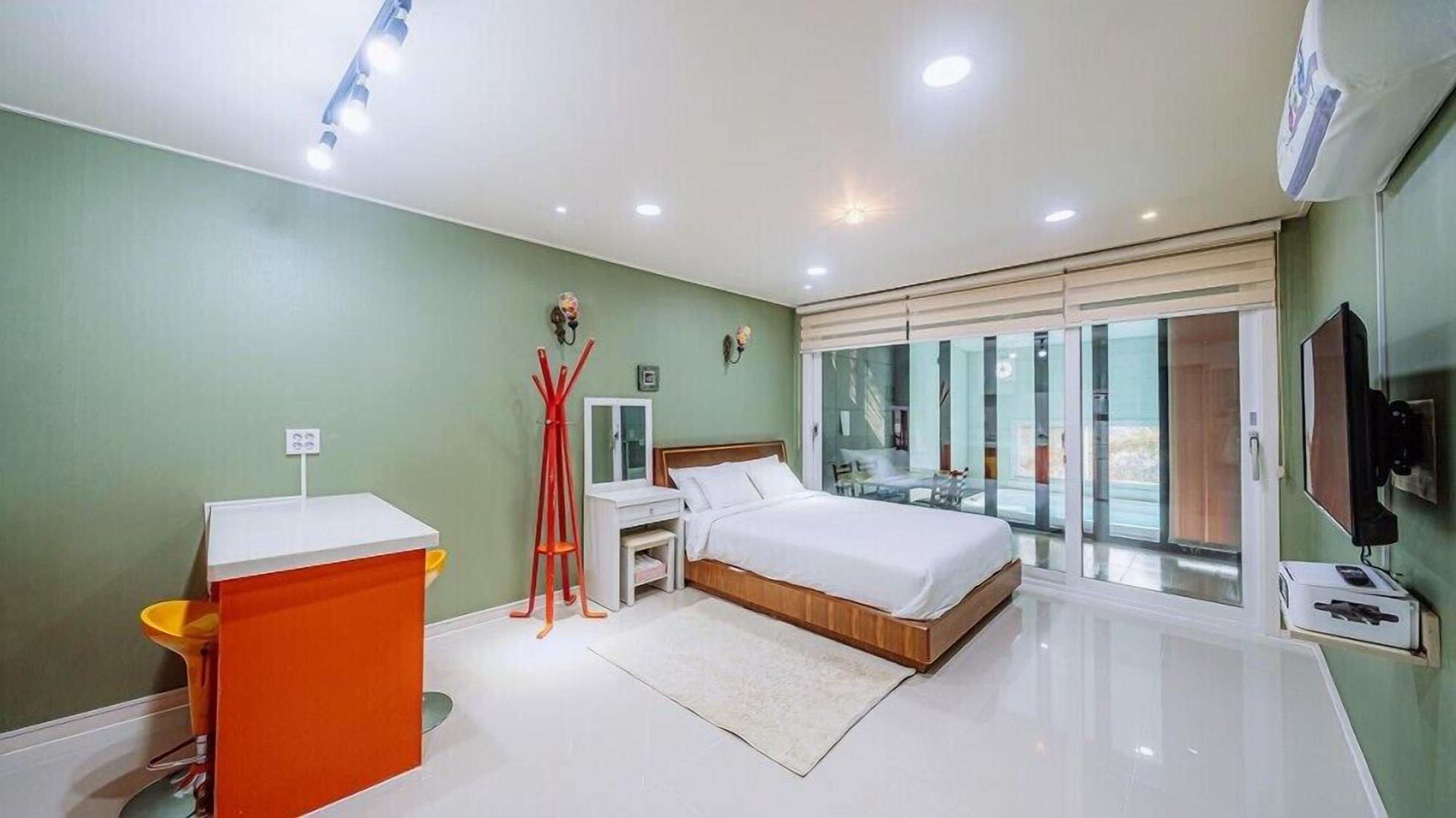 Un dormitorio moderno con cama, mesitas de noche, escritorio y un amplio ventanal.
