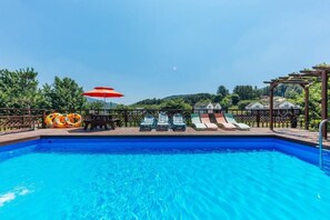 A swimming pool with lounge chairs and an umbrella, surrounded by a wooden deck and greenery. - Huenest pension (Gapyeong)