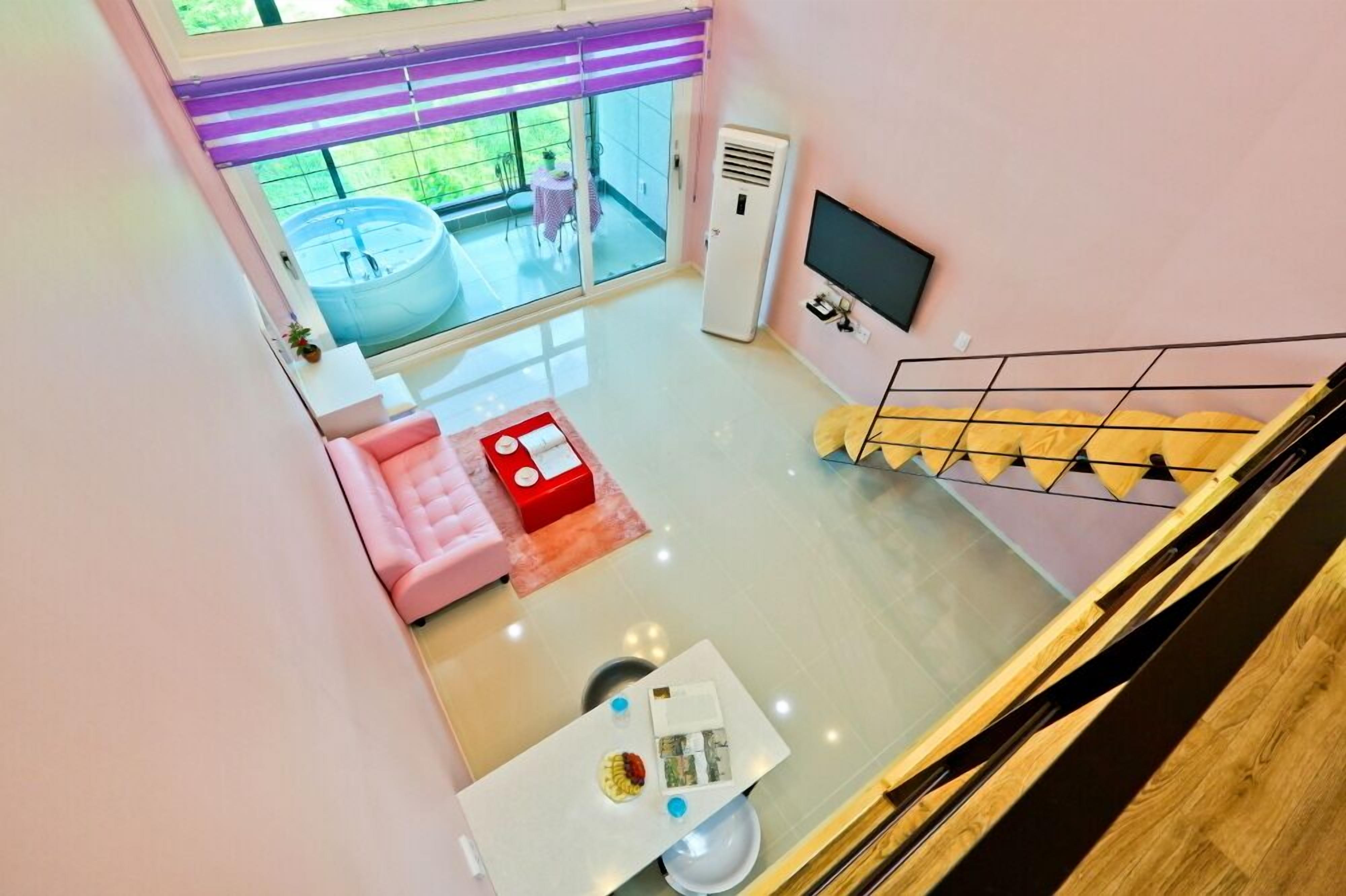 Uma sala de estar moderna com um sofá rosa, uma mesa pequena com uma caixa vermelha e uma TV na parede.
