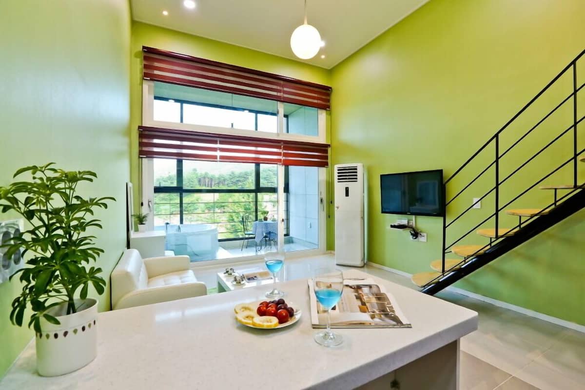 A modern living room with a dining area, a staircase, and a large window with blinds.