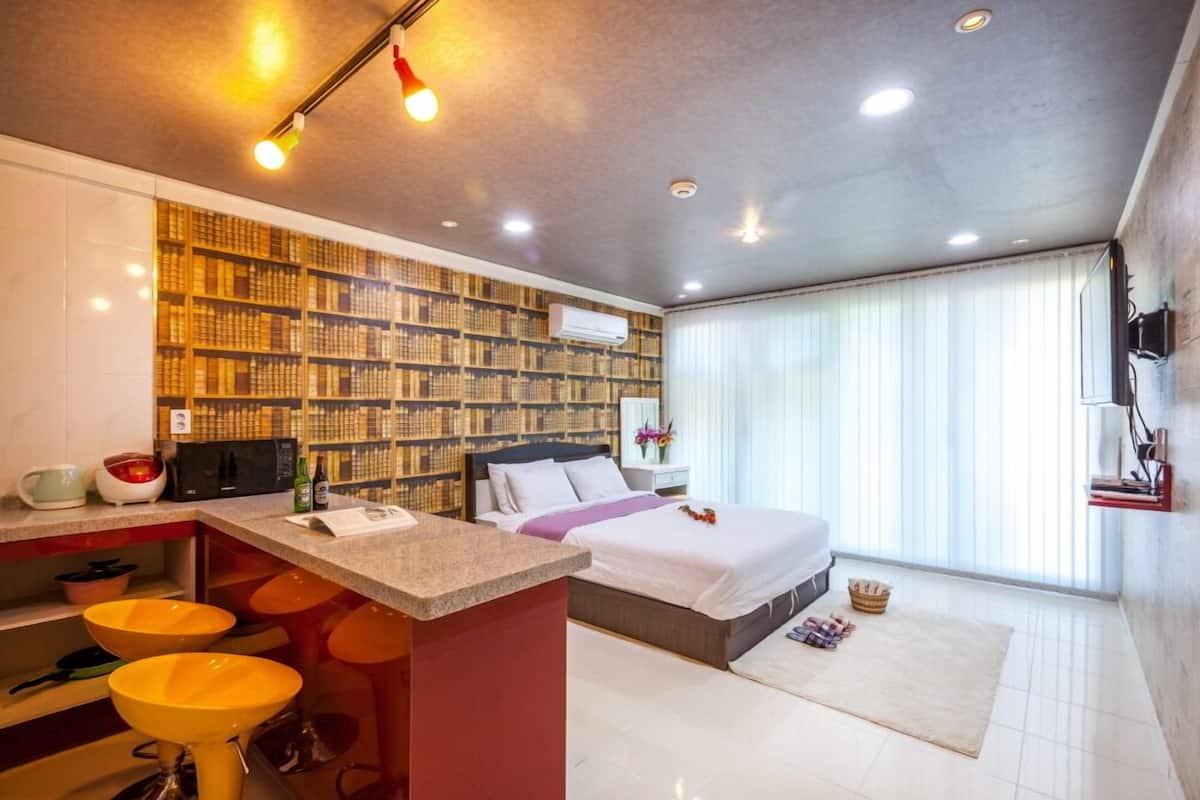 A modern hotel room with a kitchen area, a large bed, and a view of the outdoors.