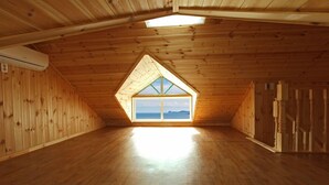 A spacious attic room with wooden walls and a large skylight window offering a view of the sky and distant landscape. - Mulbit Hanul (Geoje)