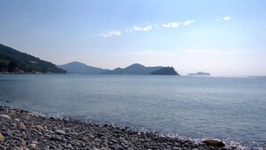 A calm lake with a pebbled shore and distant mountains. - Mulbit Hanul (Geoje)