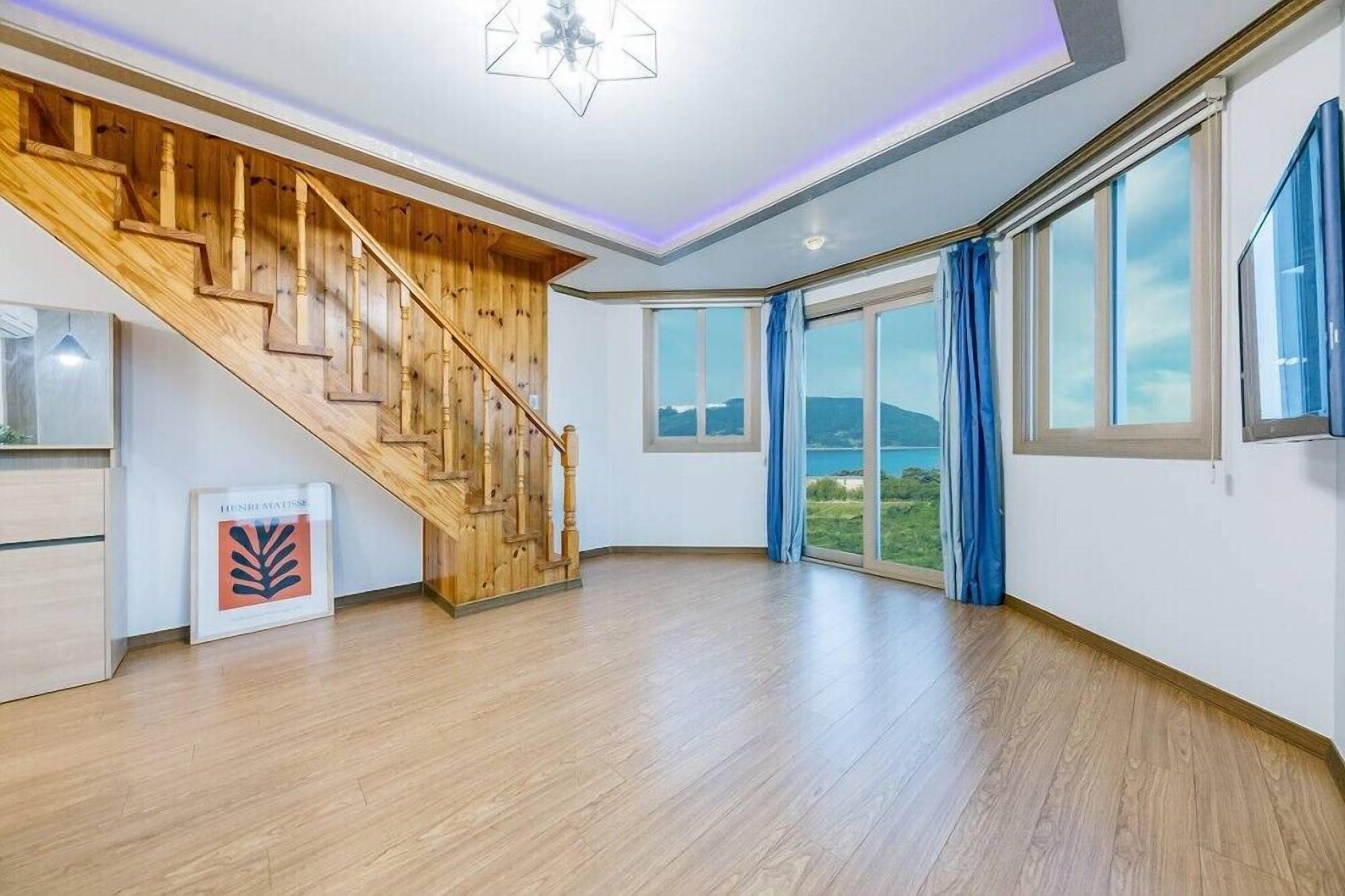 A spacious room with a wooden staircase, large windows, and a view of the outdoors.
