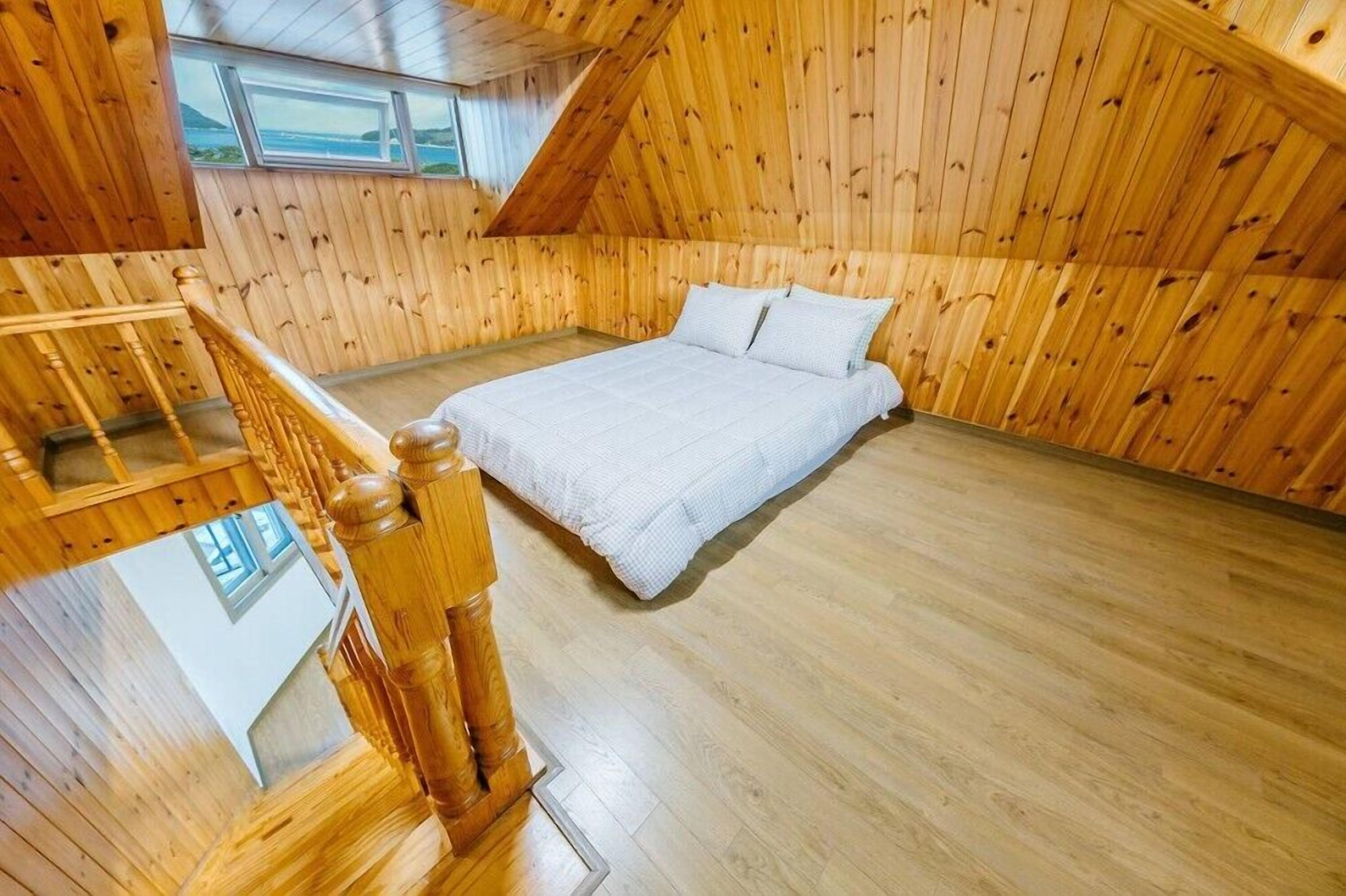 A wooden-paneled room with a bed, a wooden staircase, and a window overlooking a landscape.