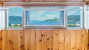 Habitación con techo de madera y un ventanal con vista a un paisaje costero.